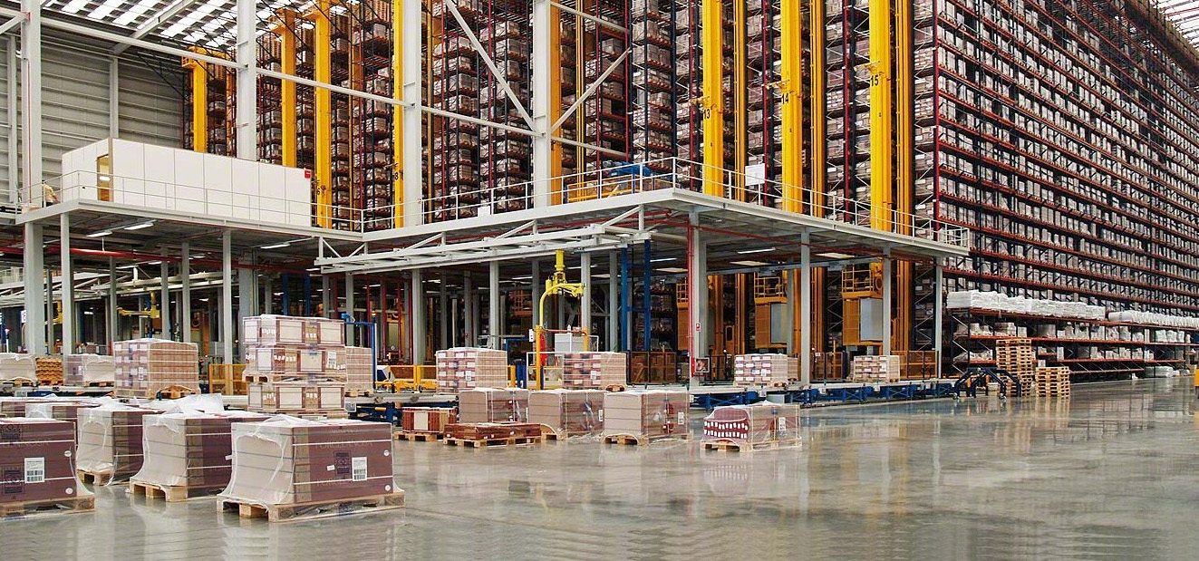 Interior de un almacén logístico automatizado de gran altura con estanterías industriales, transelevadores amarillos y palets de mercancía embalada en primer plano